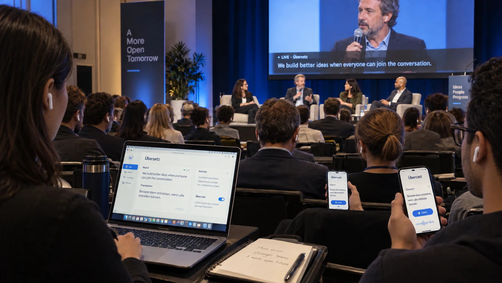 Conference panel with Übersetz on a MacBook, attendees listening on their phones and live captions on the stage display